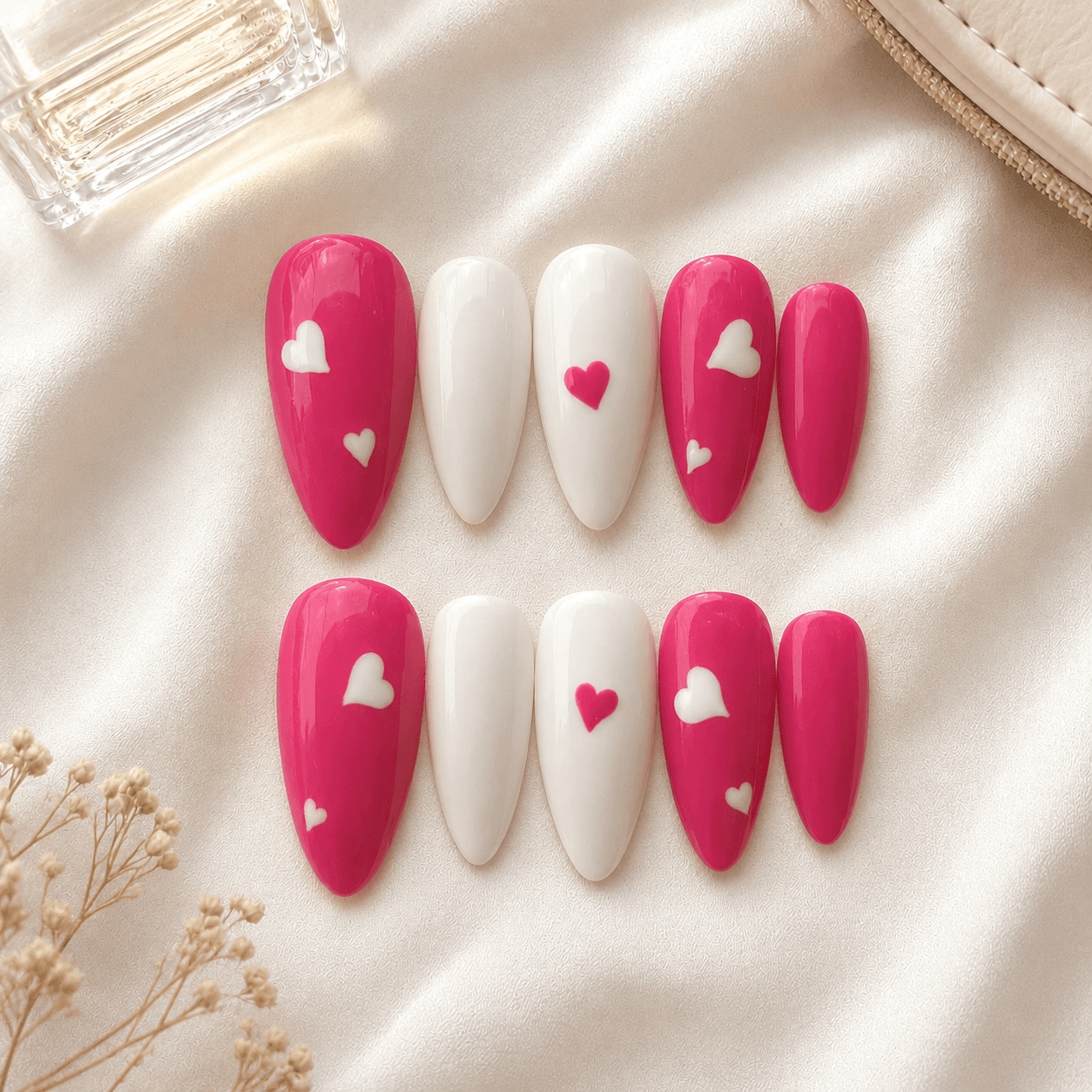 Handcrafted press-on nails with pink heart motifs on a glossy nude base.
