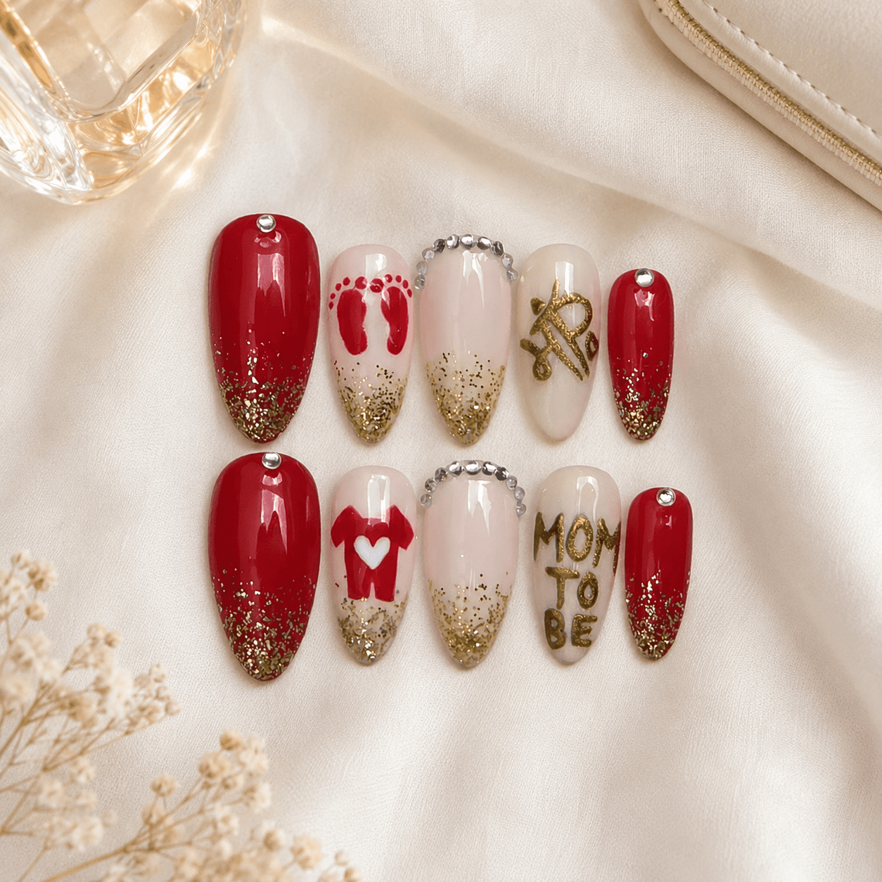 Handcrafted almond press-on nails with red, gold glitter, rhinestones, and mom-to-be details.