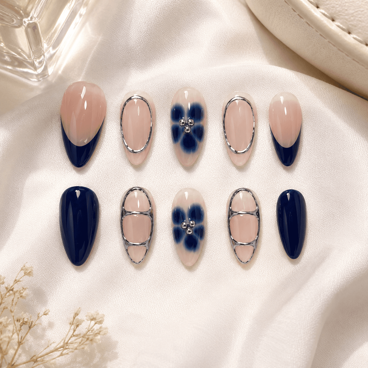 Handcrafted almond press-on nails with navy blue petals, chrome outlines, and glossy nude accents.