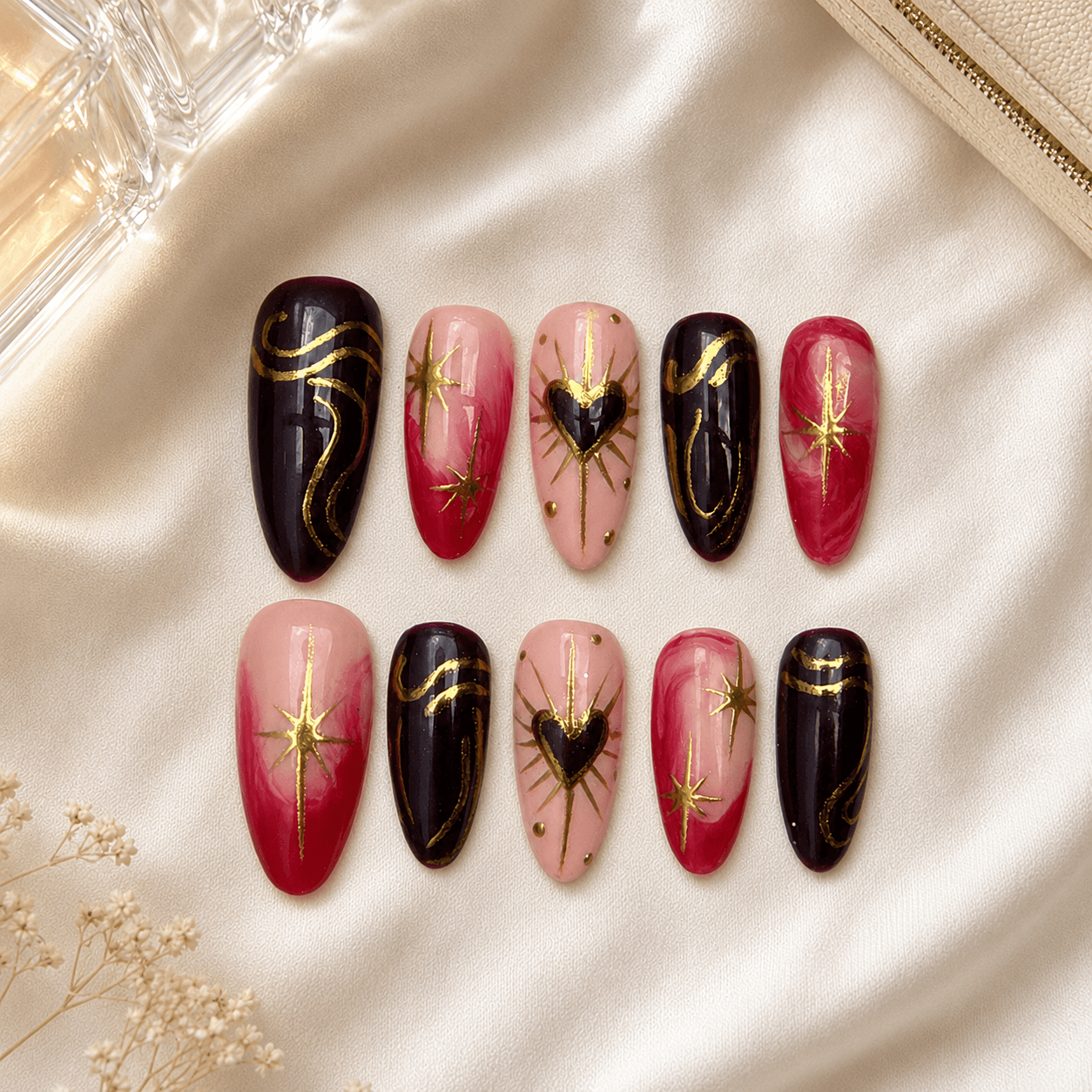 Handcrafted almond press-on nails with ruby red, black, gold starburst, and heart details.